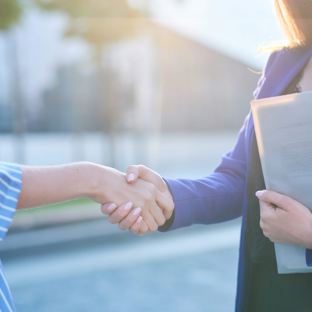Two busy businesswomen have unformal meeting outside, they are greeting one each other with handshake.